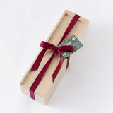 The Wood Wine Gift Box with Ribbon features a rectangular wooden design, burgundy ribbon and bow, topped with a green gift tag, set against a white background.