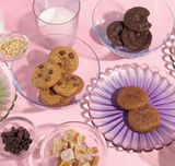 Three Chewy Chocolate Chip Cookies made with artisan red wheat flour, nuts, and milk rest on a pink table.