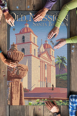 Four people assemble the 1000 Piece Santa Barbara Mission Puzzle featuring a fountain and palm trees.