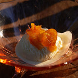 Vanilla ice cream topped with Ruby Valencia Orange and Apricot Marmalade in a glass dish on a wooden surface.