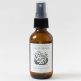 Amber bottle labeled California Room & Body Mist, clean scent, floral graphic on a white background.