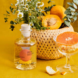 A Citrus Champagne Vinegar bottle with orange, flowers, and sliced citrus on yellow.