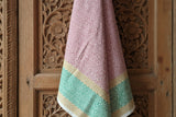 The Sunrise Fair Trade Block Printed Linen with pink and green hangs on a carved wooden floral door.