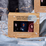 Kids Space Exploration Sock Gift Box on a soft blanket surrounded by twinkling string lights