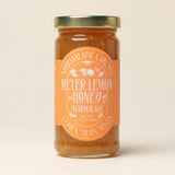 A jar of Meyer Lemon & Honey Marmalade with an orange label and gold lid on a plain background.