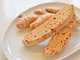 Enjoy two Ginger Spice Biscotti slices and ginger root on a white plate from our artisan bakery.