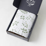 An open Santa Barbara Wine Gift Box wrapped in green leafy paper with a gourmet treat from Margerum Winery inside.
