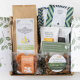 Savor Snack Box: Includes tea, dried apricots, cookies, almonds & organic dried mango on a leafy background.