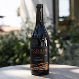 A Stolpman Hilltops Syrah bottle rests on a stone surface with blurred greenery in the background.