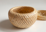 The Petite Woven Basket, with a matching lid, is a versatile handmade piece shown on a plain white surface.