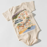 Carly's Santa Barbara Map Onesie is cream-colored, made from organic cotton, and features a colorful illustrated map of Santa Barbara with landmarks, palm trees, and the beach. It has short sleeves and snap buttons at the bottom.