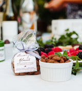 A bag of Chocolate Dusted Caramelized Almonds sits beside a bowl, with berries and mint in the background.