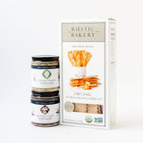 A box of Crackers & Spreads sits next to two jars of tapenade—Artichoke Parmesan and Kalamata Olive—against a white background.