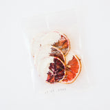 Three Creme Blood Orange Crisps, half-dipped in creme chocolate, in a clear bag on a white background.