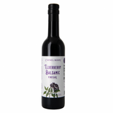 A dark glass bottle of Elderberry Balsamic Vinegar with a white label, purple text, and an illustration of upcycled elderberries and green leaves.