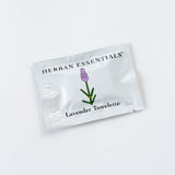 A white packet labeled Lavender Essential Oil Towelettes, with a lavender illustration, rests on a plain white surface—ideal for your travel kit as a soothing essential oil wipe.