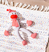 The Monkey in PJs Organic Cotton Stuffed Toy rests on a textured white rug with colorful specks and fringe, which is placed atop a wooden floor.