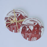 The Old Santa Barbara Mission Letterpress Coasters are two round cotton coasters featuring a reddish-brown illustration of the mission. One is tied with raffia, both rest on a light background, showcasing artisanal letterpress print for charm.