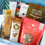 The Petite Coffee and Tea Gift Box includes biscotti, a macadamia nut bar, Little Apple snacks, Copper Cow Vietnamese Pourover Coffee, and organic tea packets, all beautifully arranged with shredded paper filling.