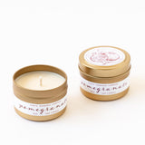 Two small travel-sized tins labeled Pomegranate Travel Candle, one open to show the white soy wax and one closed with a lid featuring a pomegranate illustration, from Santa Barbara Company.