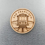 The San Francisco Trolley Wood Magnet features an engraved trolley, train tracks, and "San Francisco," displayed against a gray textured background.