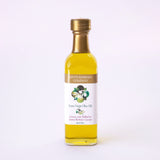 A clear glass bottle of Santa Barbara Extra Virgin Olive Oil Sampler with a gold cap and a white label featuring an olive branch stands upright on a white background. Crafted in the Santa Ynez Valley.
