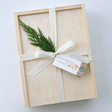 The Santa Barbara Olive Oil & Vinegar Gift Box, presented in a wooden box with a cream ribbon, pine sprig, and Santa Barbara Company tag, showcases premium olive oil from Santa Barbara County on a white background.