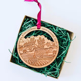 The Santa Barbara Wine Country Wood Ornament, engraved with a vineyard scene and "Wine Country Santa Barbara, CA," comes in a box with green shredded paper and has a pink ribbon for hanging—perfect as a charming holiday keepsake.