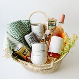 The Santa Barbara Wine Picnic Basket features a bottle of rosé, two Aura Bora cans, white tumblers, a green patterned cloth, organic pistachios, gold bottle opener, and yellow flowers—an ideal chic gift for any beach picnic.