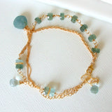 The Seaside Moss Gold Bracelet features clusters of faceted and round moss aquamarine and blue topaz beads on a 14k gold fill chain, beautifully displayed on a white textured surface.