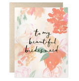 The To My Beautiful Bridesmaid Card by Heiday is an A2 blank card featuring pastel pink, peach, and orange flowers with green leaves. Handwritten text reads "to my beautiful bridesmaid." Includes a partially visible gold envelope.