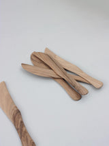 Five hand-carved Walnut Wood Knives are stacked on a light gray surface, with one knife placed separately to the left.