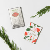 Happy holidays Floral Blooms Box Set with a sailboat chocolate bar next to a gold foil holiday greeting card.