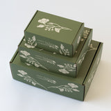 exterior of sage green mailer gift boxes showing California poppy graphics and santa barbara company logo