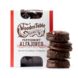 A box of Peppermint Chocolate Alfajores Cookies beside mint chocolate cookies with dulce de leche and red sprinkles.