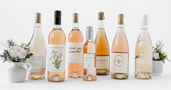 Seven bottles of Rosé with small cups of flowers on either end