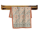 Sienna Earth Block-Printed Kitchen Towel with florals and red border, hanging on a wooden rack.