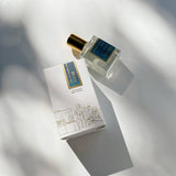 Blue Perfume Oil roll-on with blue and gold labels and white box rests on a sunlit white surface.