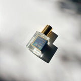 Blue Perfume Oil’s small roll-on bottle with gold cap casts a shadow on white in bright sunlight.