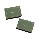 Two olive green Matchbox Cheers with a scalloped border and gold CHEERS! text, perfect as a thoughtful dinner party favor.