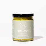 A glass jar of Zucchini Pesto with a black lid and light green label, displayed on a white background.