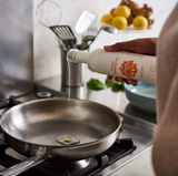 Someone pours Algae Cooking Oil into a pan on the stove in a sleek, modern kitchen.