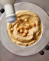 Hummus topped with chickpeas, spices, and heart-healthy Algae Cooking Oil being poured from a bottle.