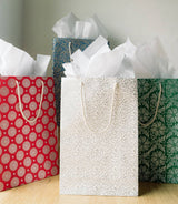 Four Recycled Paper Medium Holiday Gift Bags 7x3.5x10 - Assorted in red, blue, green, and white, filled with tissue paper.