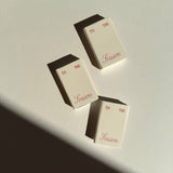 Three cream-colored Matchbox Tis The Season favors, each printed with the text TIS THE Season in red.