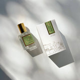 Sunday Olive Perfume Oil and its box rest on a white surface with soft, leafy shadows cast across them.