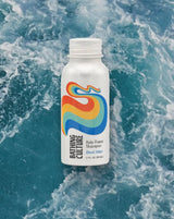 Kelp Forest Shampoo Travel Size, with a colorful wave design, floats above a blue wavy water background.