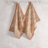 Two Sienna Earth Block-Printed Kitchen Towels with floral motifs and orange borders hang side by side on hooks.