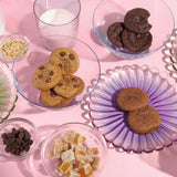 Chewy Oat Cranberry Cookies served on pastel plates over a pink background with nuts, chocolate chips, and milk.