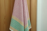 A Sunrise Fair Trade Block Printed Linen towel in pink, green, and beige hangs on a wooden door.